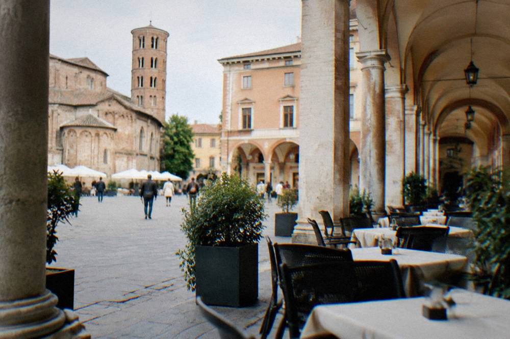 A busy Italian square with cafe tables under arcades in late afternoon light