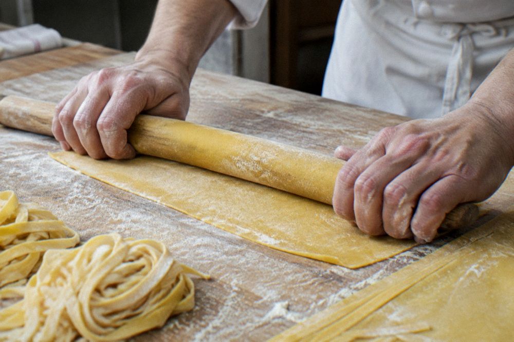A chef rolling fresh egg pasta dough on a floured wooden board