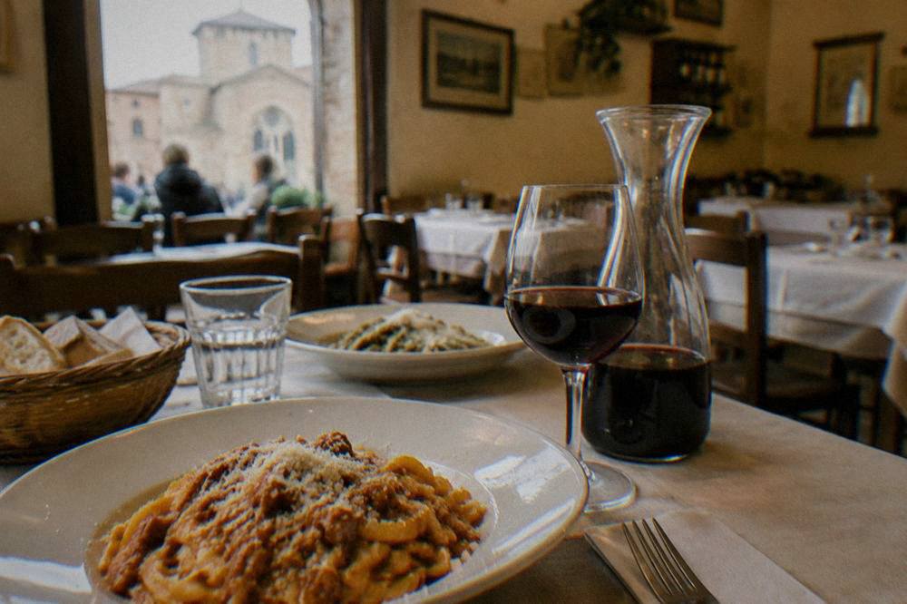 A table set with pasta dishes and a carafe of red wine inside a small trattoria