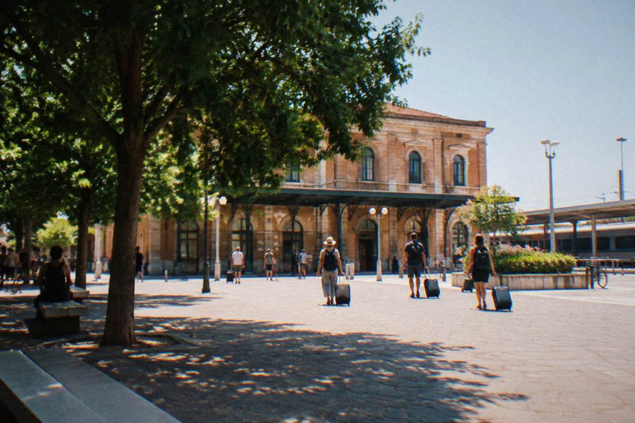 The station forecourt in Ravenna with the station building and passengers with luggage