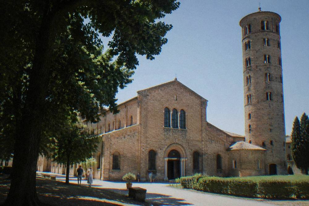 Exterior of a brick basilica with a round bell tower under a clear sky in Ravenna