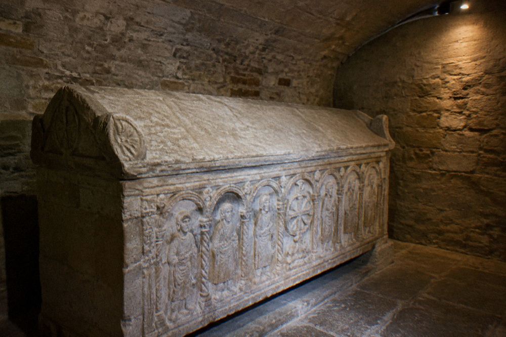 A stone sarcophagus tomb in a quiet small stone chamber lit by a lamp