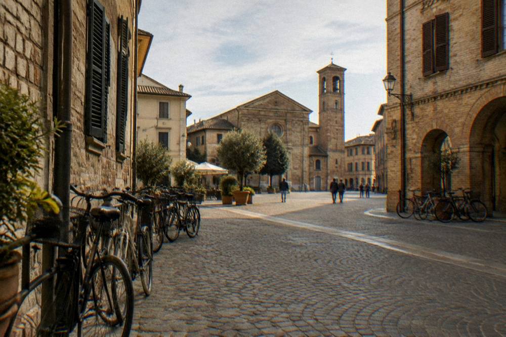 A cobbled square in an old Italian town centre with parked bicycles and shuttered facades
