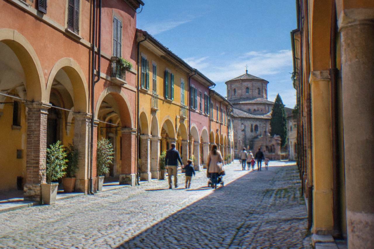 Families walking a cobbled street of coloured porticoed houses in Ravenna