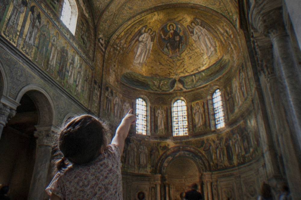 A child pointing up at a golden mosaic ceiling inside a Ravenna church