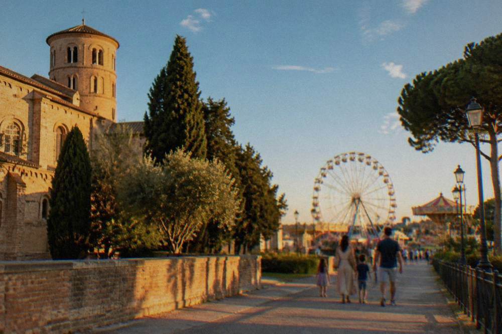 A family walking a wide path toward amusement park rides under a blue sky
