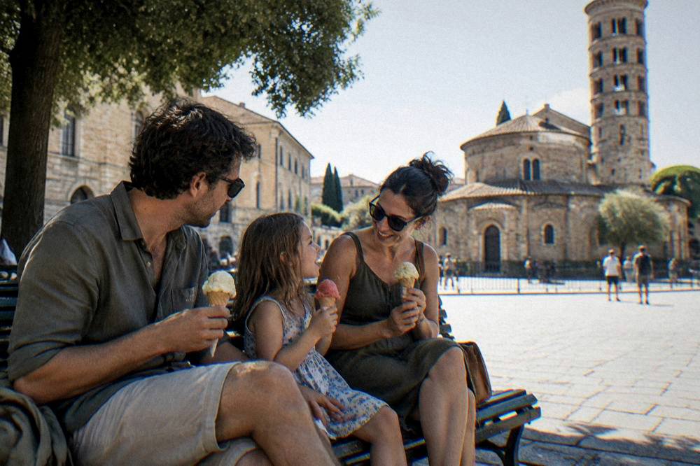 A family sharing gelato on a bench in a sunlit Italian square