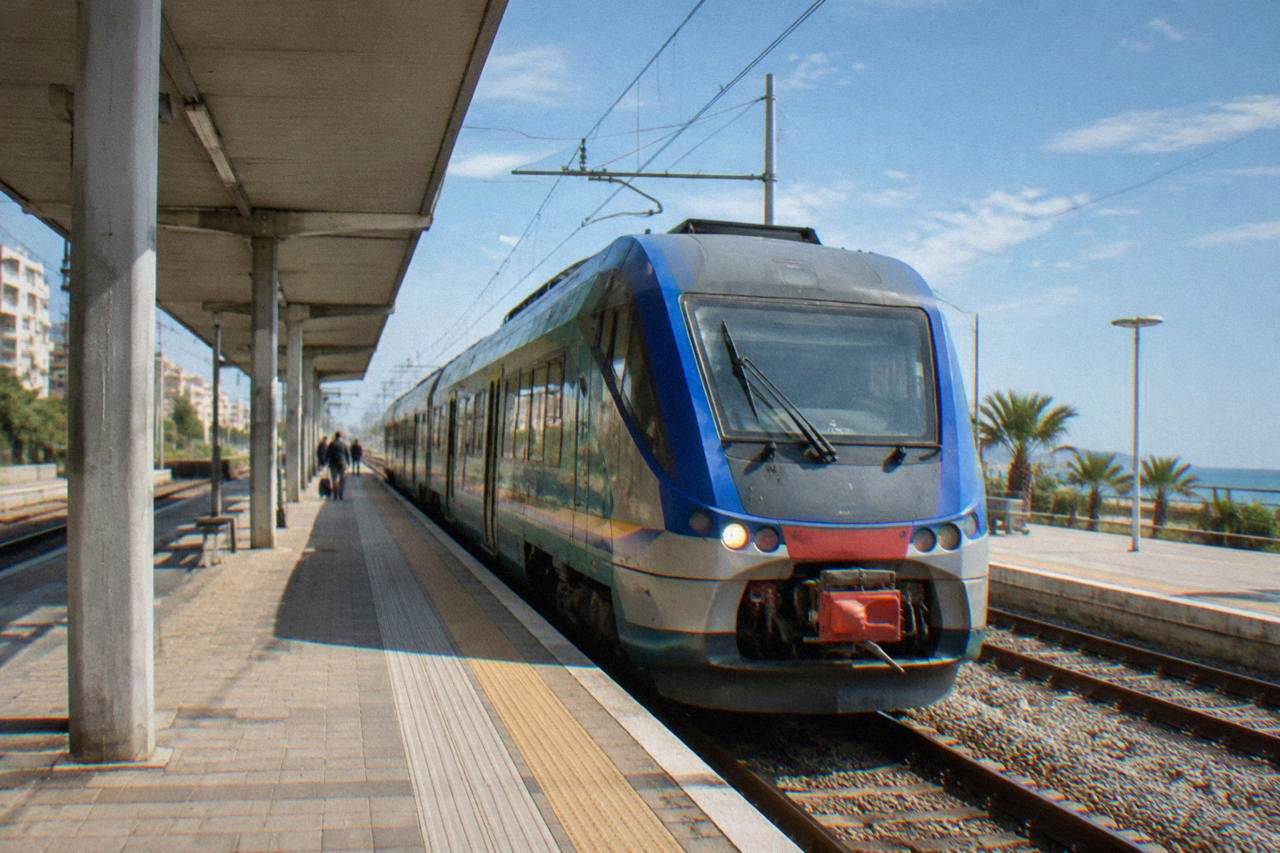A regional train waiting at an Italian railway station platform on a bright morning
