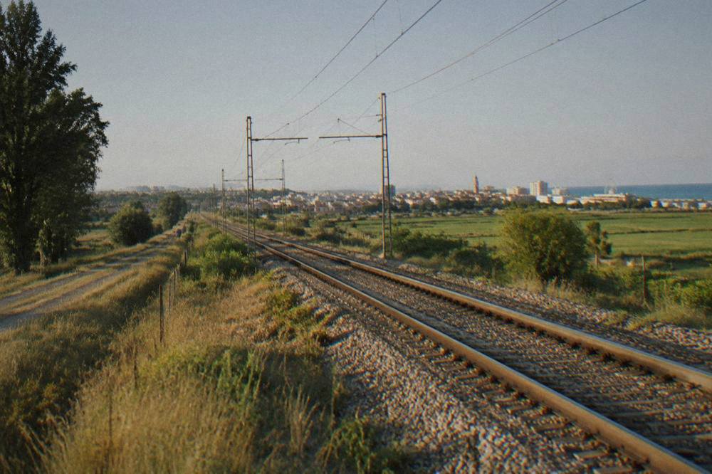 Railway tracks running through flat countryside towards a distant Italian town
