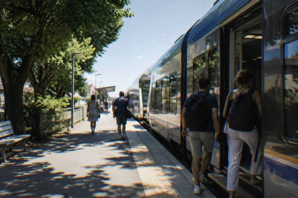 Passengers boarding a regional train at a small Italian station with a blue sky