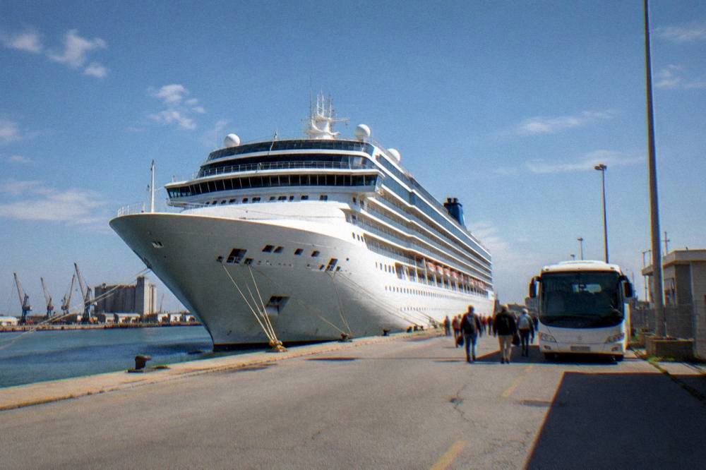 Cruise ship docked at a small industrial port with a shuttle bus waiting nearby