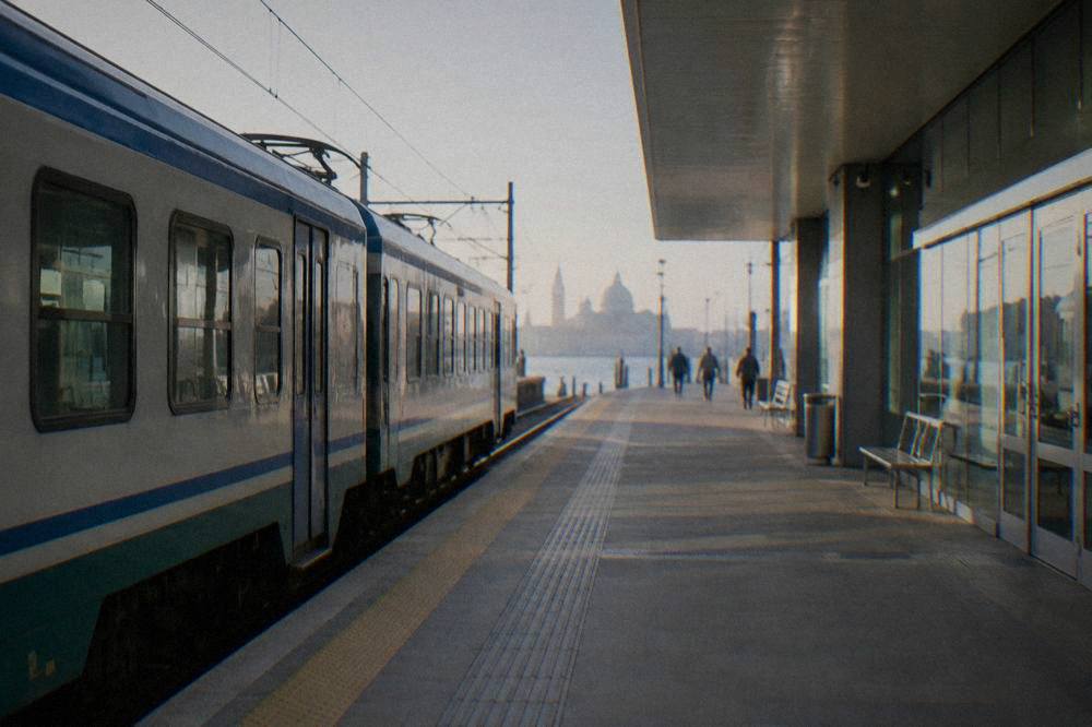 A regional train waiting at an Italian station platform beside a modern station building