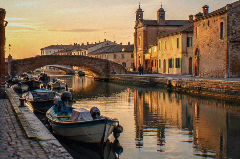 Small boats moored along a canal in a lagoon town with brick bridges