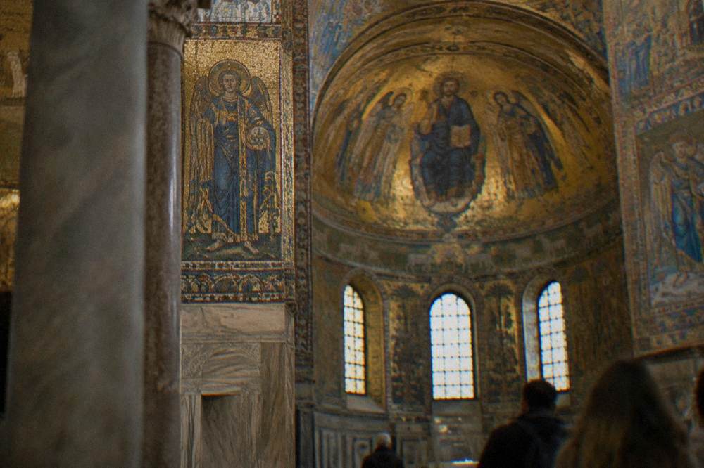 A gold mosaic interior of an ancient chapel lit softly with figures in blue and gold