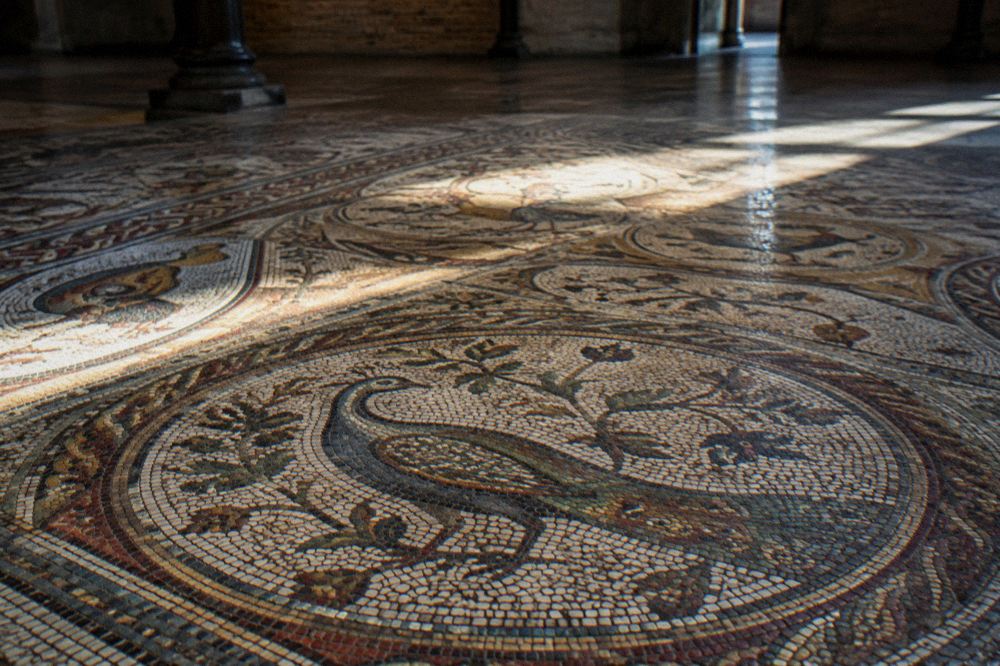 Sunlight falling across a mosaic floor of coloured ancient tiles in a dim museum hall