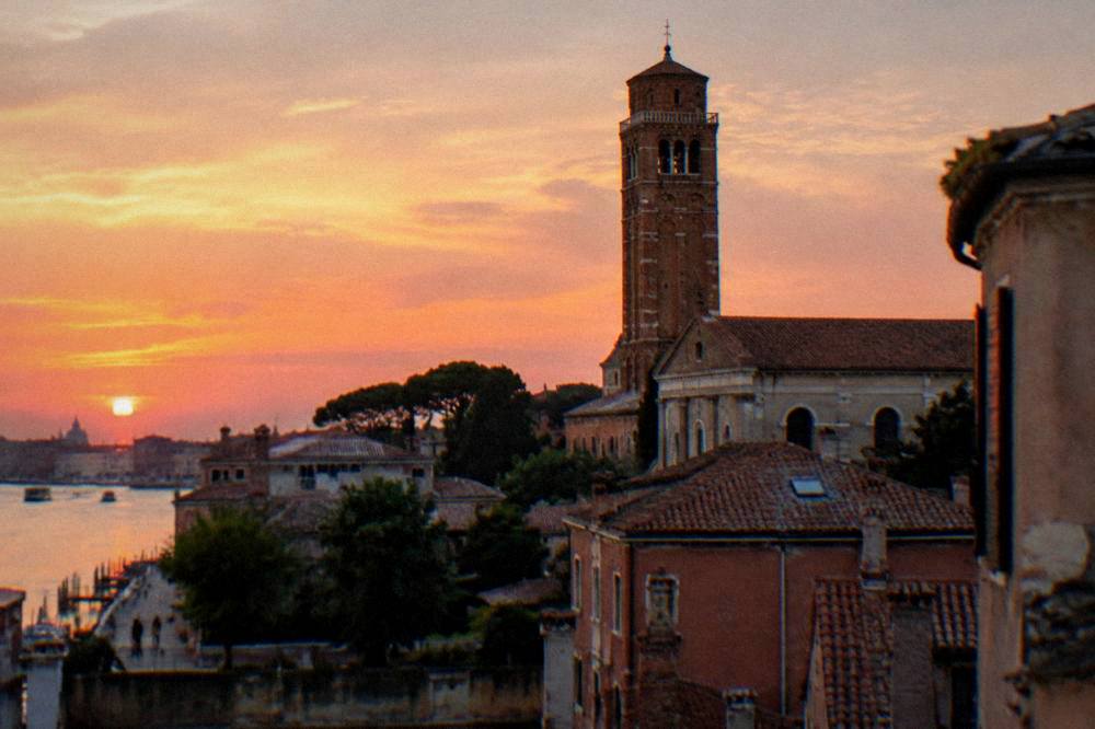 An evening view of a brick basilica bell tower above rooftops in a small Italian city