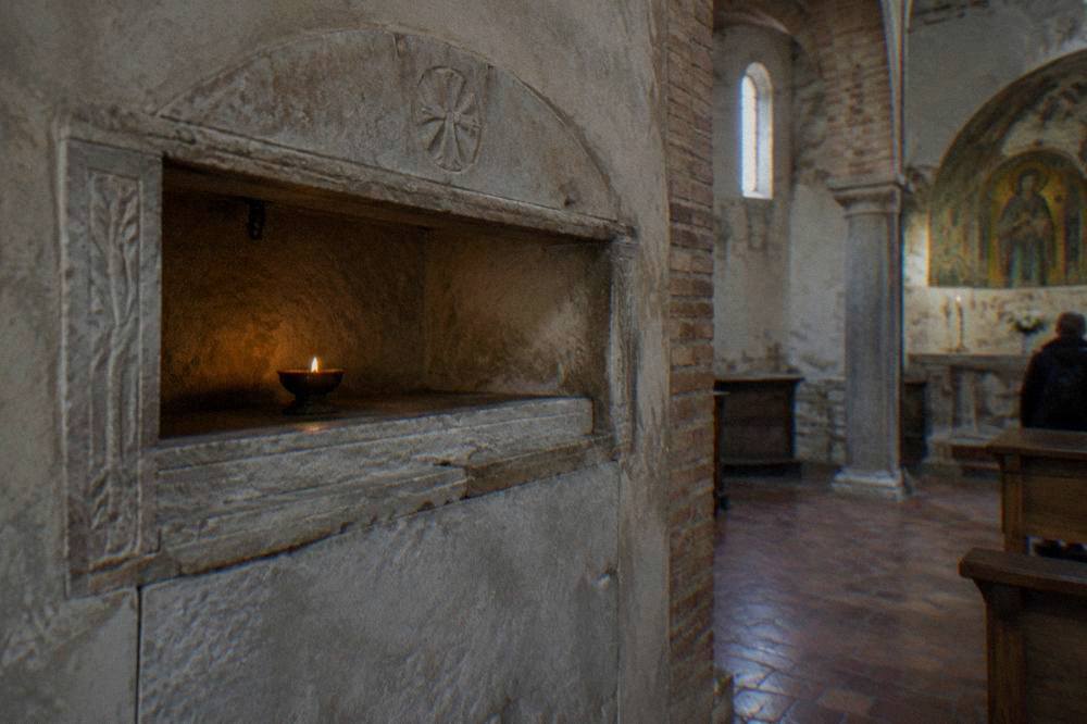 A stone tomb niche with a burning oil lamp inside a quiet small chapel