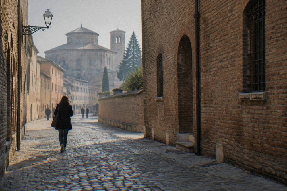 A visitor walking a cobbled street in the flat historic centre of Ravenna past brick facades