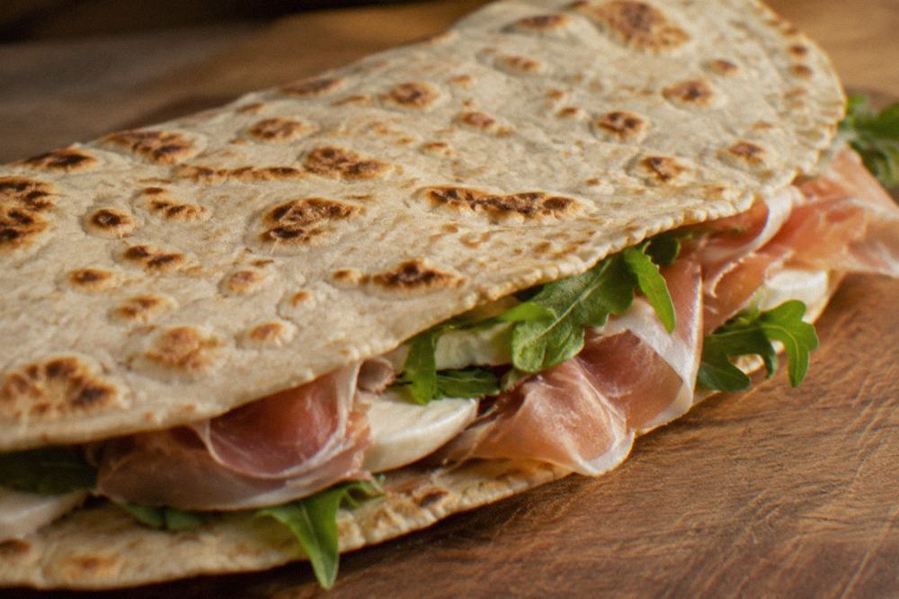 A flat griddled piadina bread folded around filling on a counter in an Italian bakery