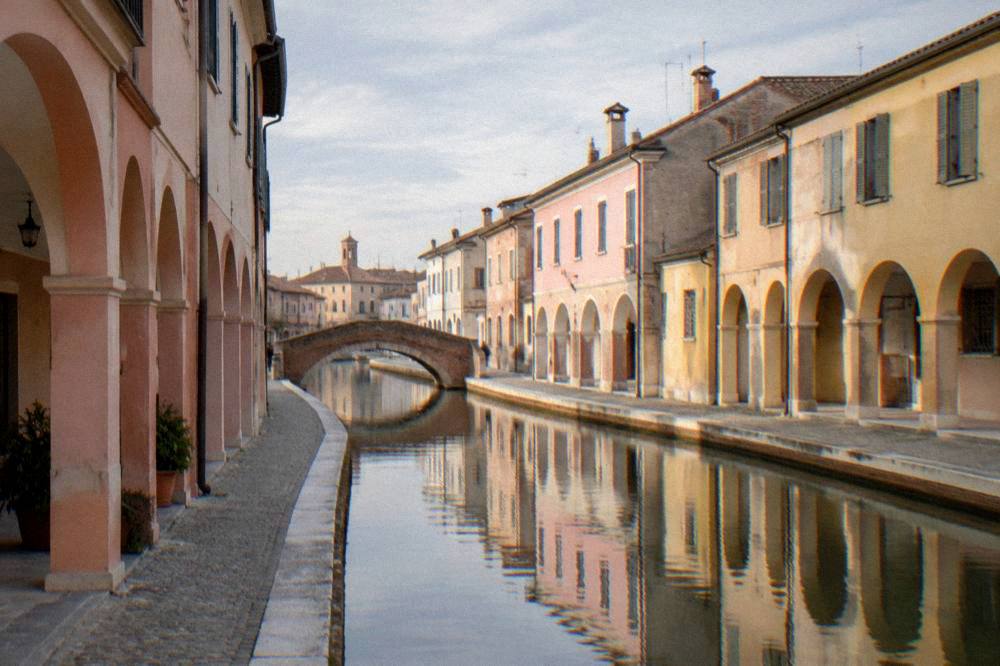 Pastel-coloured arcades and reflections along a canal in Comacchio