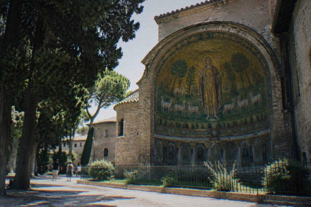 A green and gold mosaic apse showing a saint standing among sheep and trees