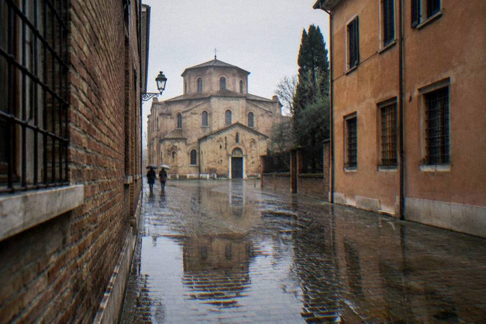 Rain-wet cobblestones reflecting the facade of an old Italian church in a narrow street