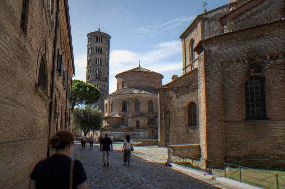 Visitors walking a cobbled Ravenna street between brick church facades
