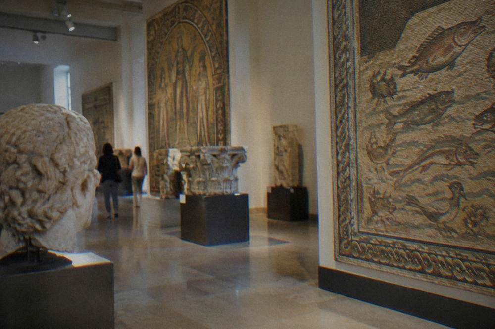 Museum gallery in Ravenna with stone artefacts and mosaic panels displayed under ceiling lights