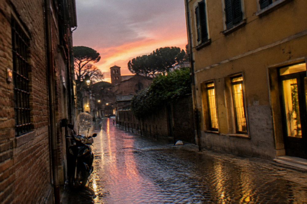 A rainy evening street in Ravenna with lit shop windows reflecting on wet cobblestones