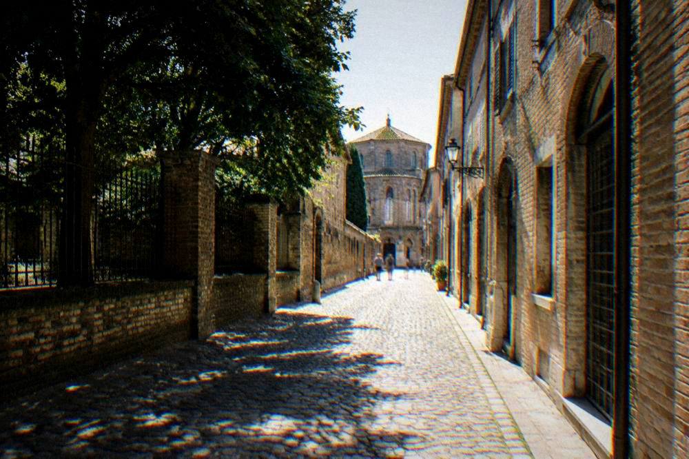 A narrow cobbled street in Ravenna lined with old brick buildings under a soft sky