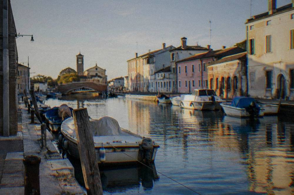 A canal-side view of a small lagoon town with boats moored along the water