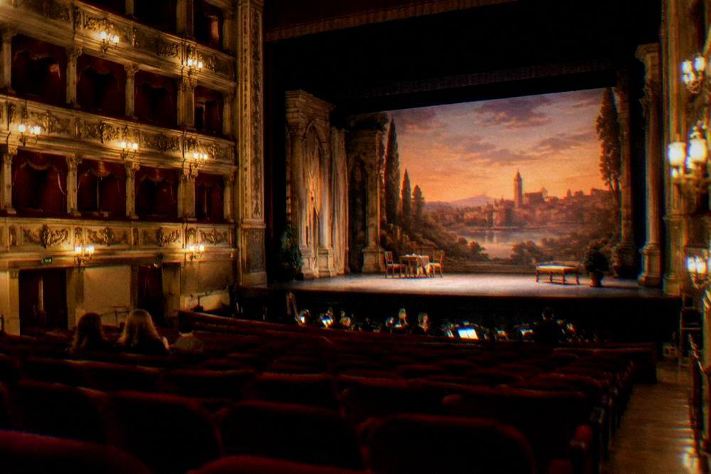A theatre interior with red seating and an ornate stage preparing for an evening performance