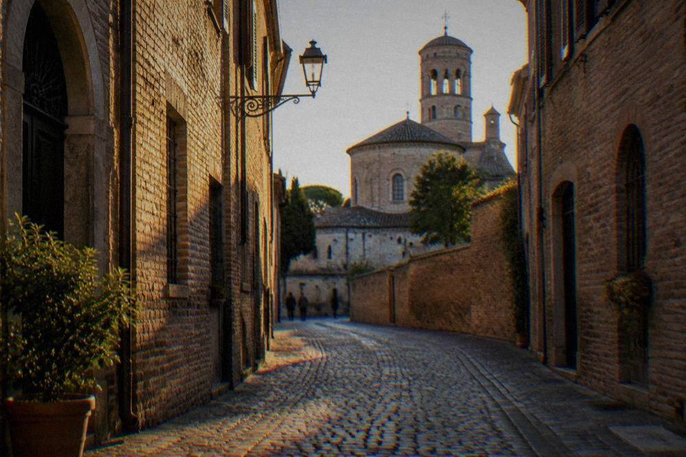 A narrow cobbled Ravenna street lined with old brick buildings in morning light