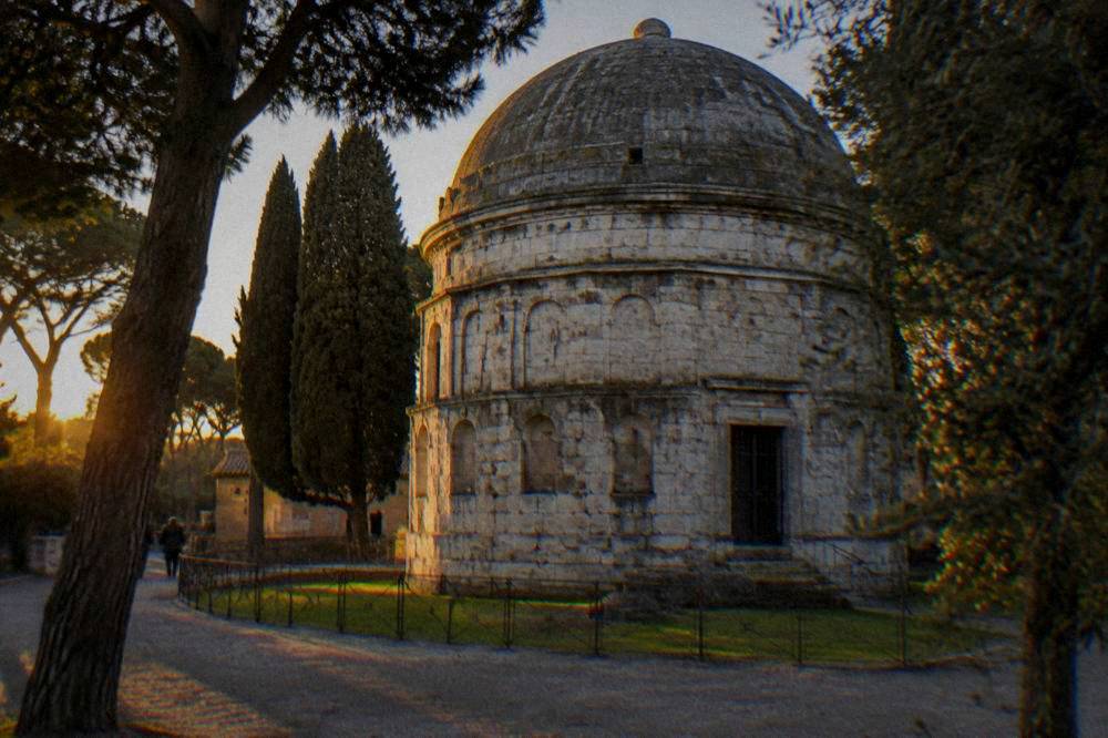 An ancient stone mausoleum with a massive domed roof standing among trees