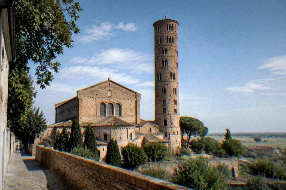 A tall ancient basilica with a brick bell tower rising above flat countryside