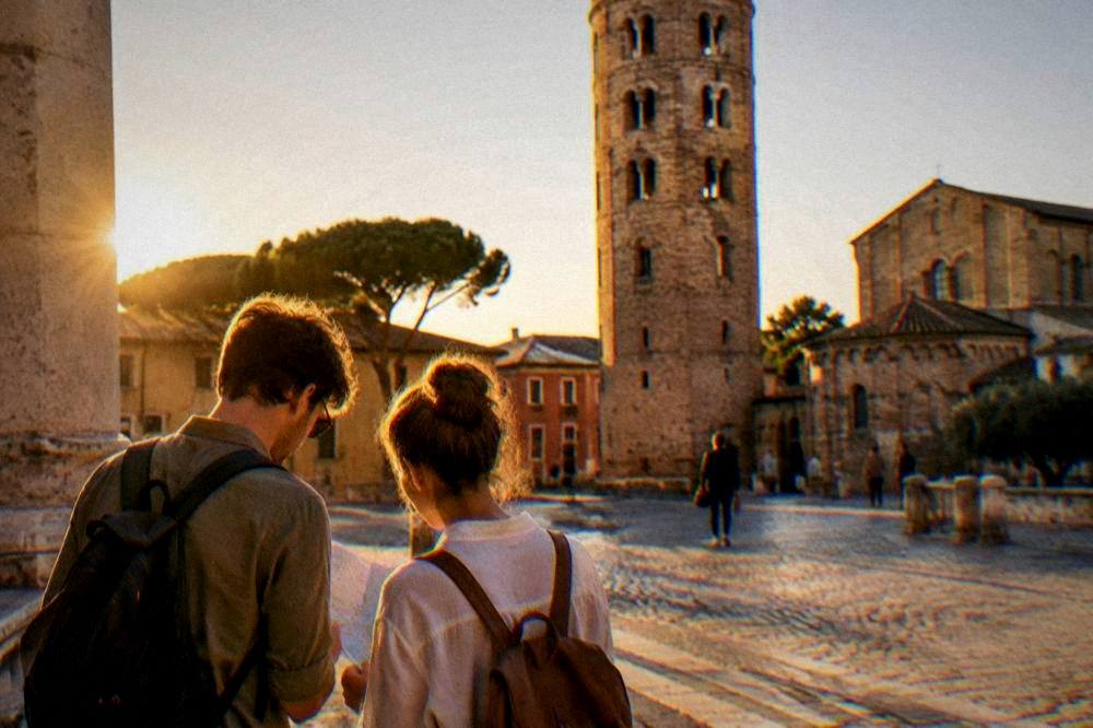Travellers reading a map on a sunlit square beside an old bell tower