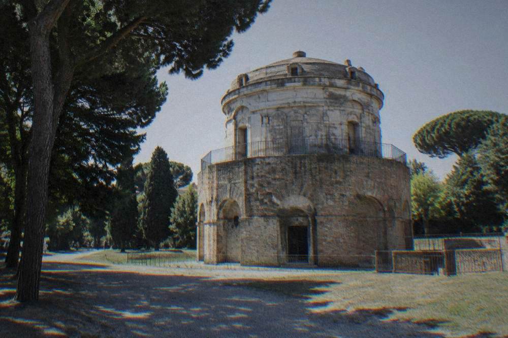 The brick exterior of the Mausoleum of Theodoric in Ravenna under a clear sky with trees around it
