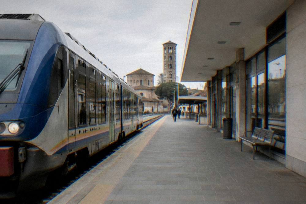 A regional train waiting at a small Italian railway station platform beside a modern station building